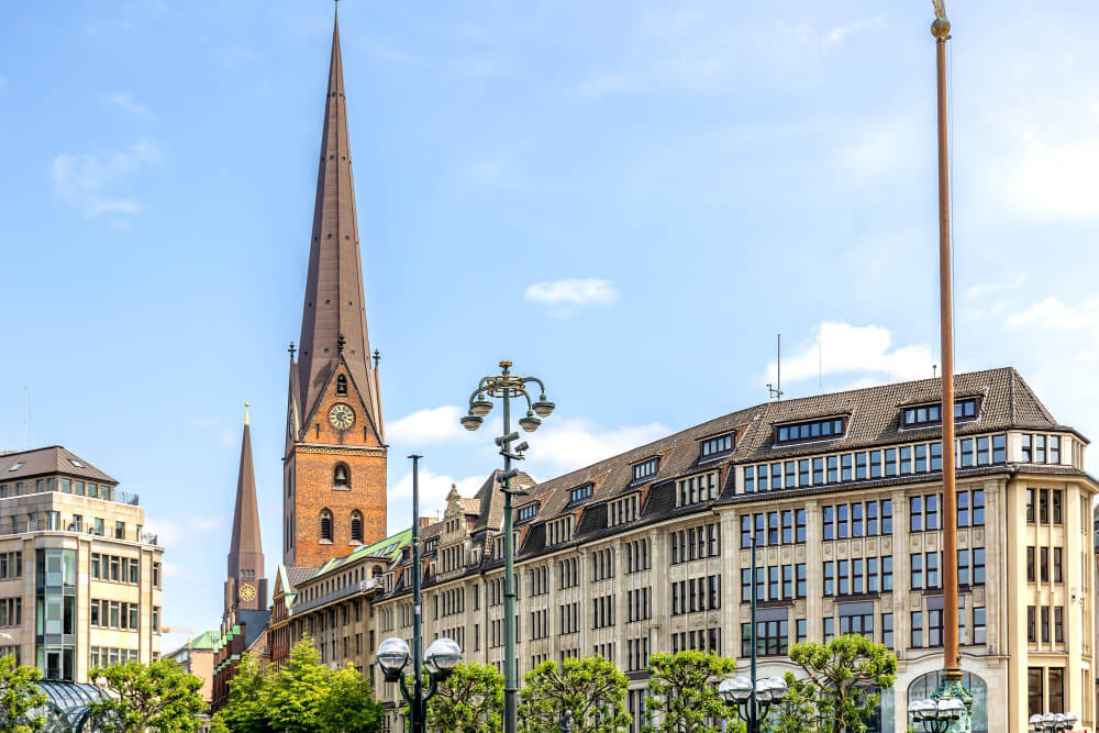 Eine hohe Kirchturmspitze erhebt sich über historische Gebäude unter blauem Himmel in einer europäischen Stadt